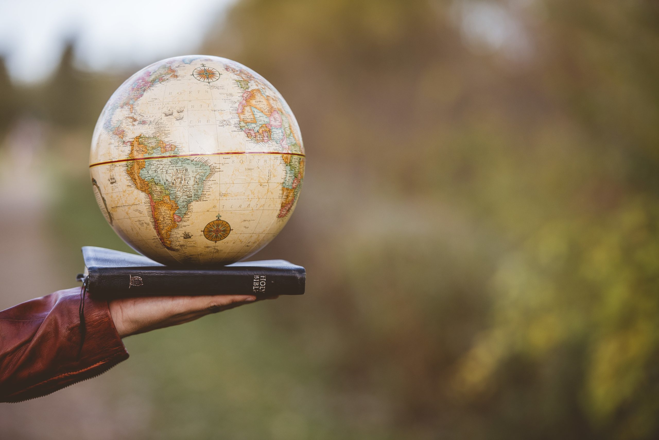 closeup-shot-of-person-holding-bible-with-desk-globe-on-top-min
